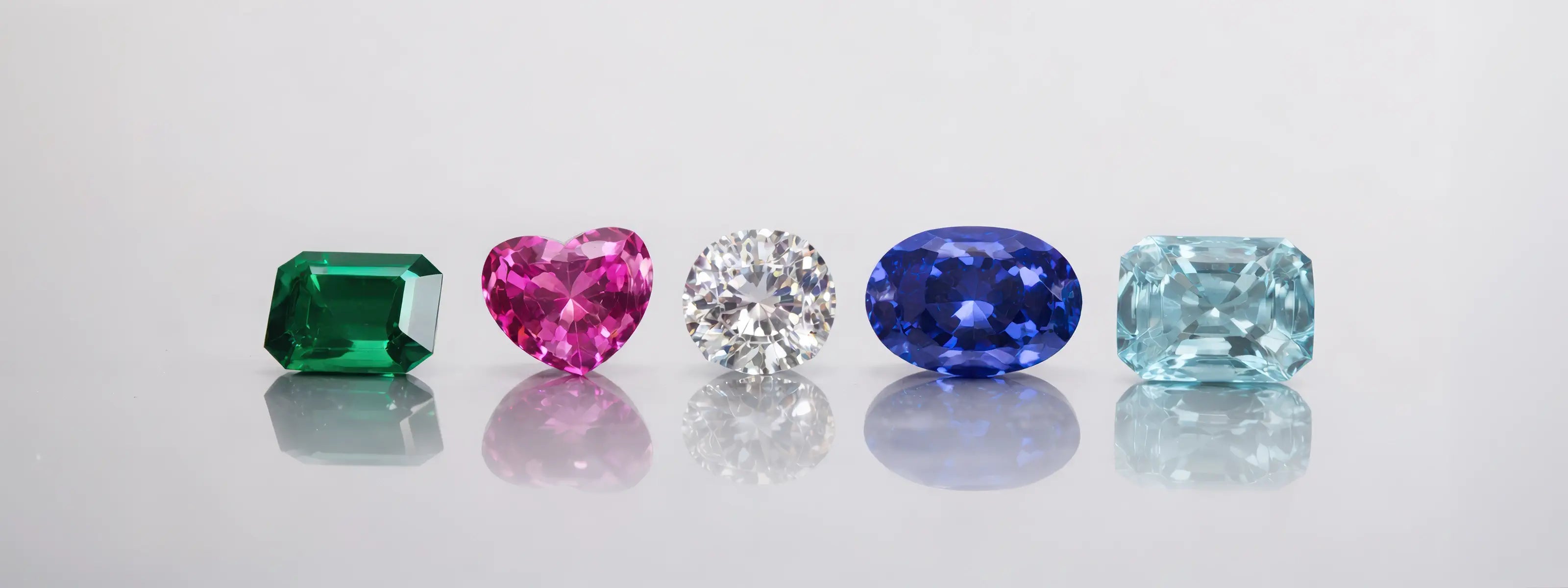 Cinq pierres précieuses colorées sur une surface réfléchissante avec un fond gris clair.