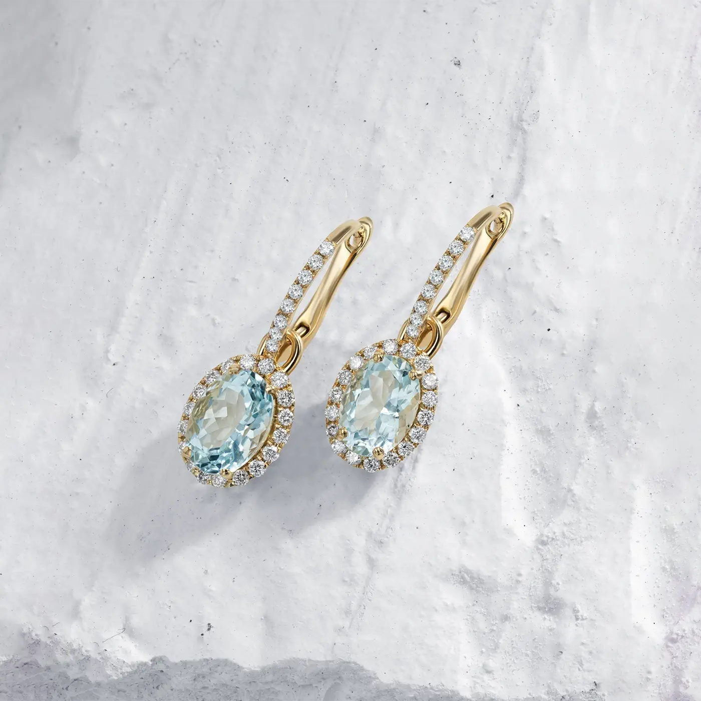 18k yellow gold earrings with aquamarine gemstones on a textured white surface