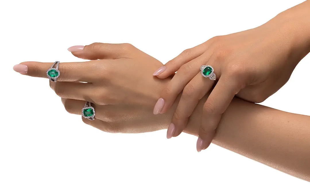 Two hands wearing emerald green gemstone rings on a white background