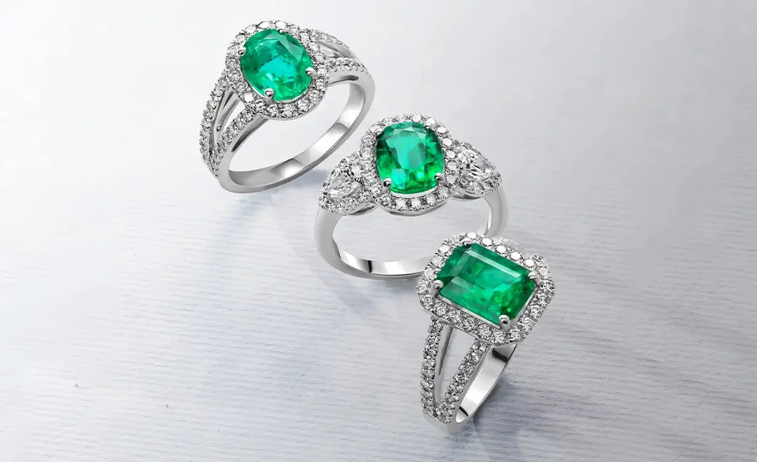 Three emerald rings on a reflective silver background
