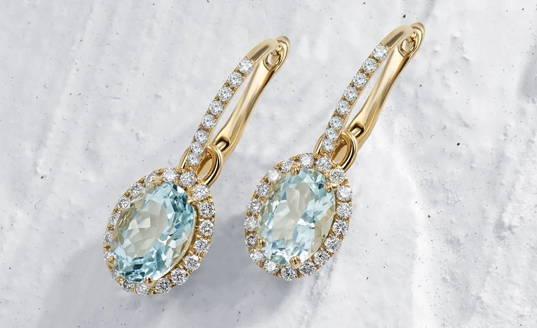 Sunrise, 18k yellow gold earrings with blue aquamarine gemstones on a textured white background